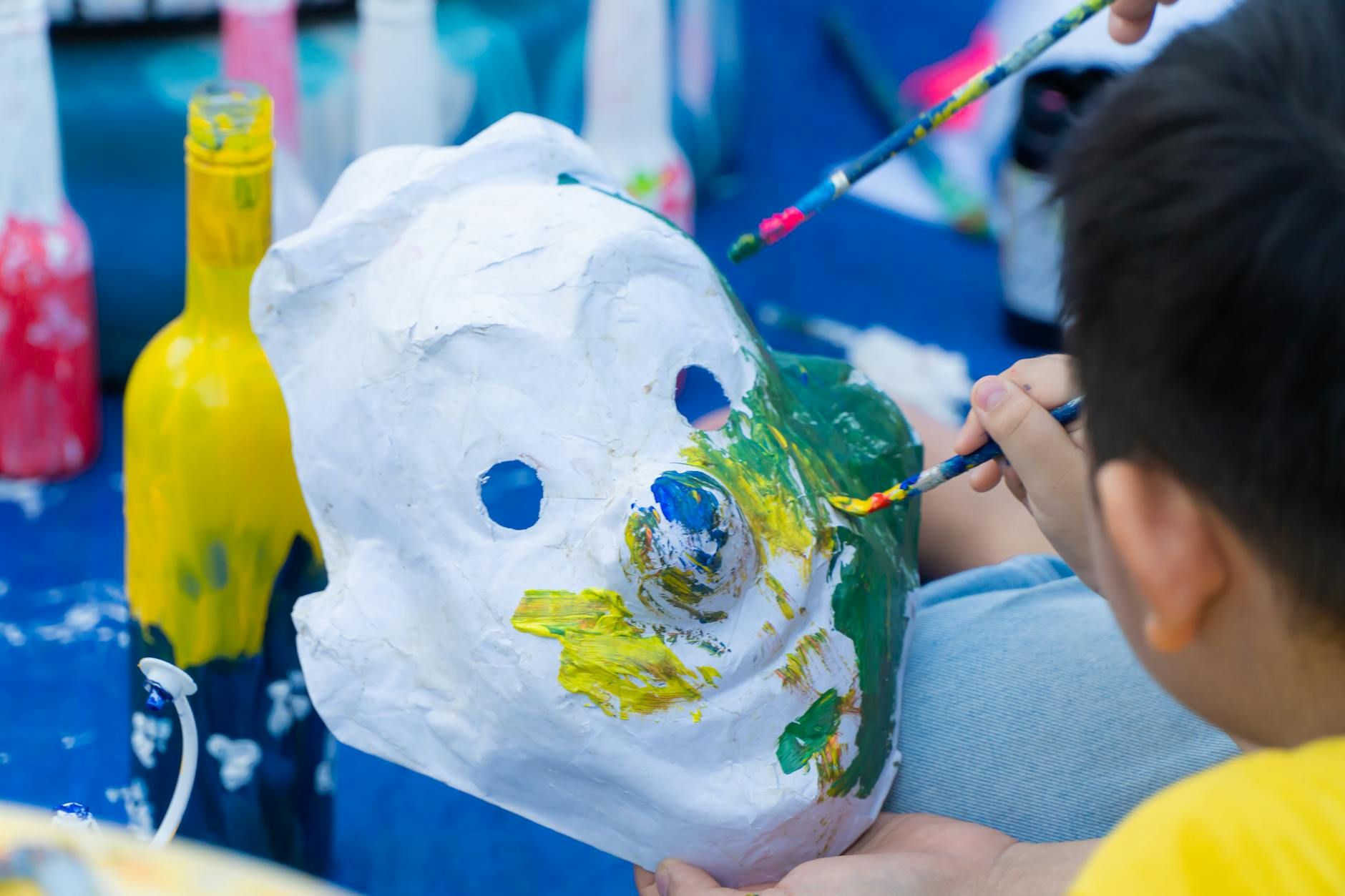 Дети раскрашивают маски за длинным столом на летнем мероприятии